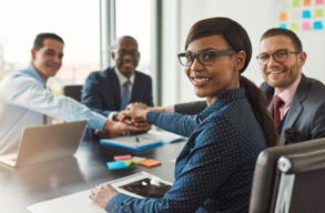 Successful African American team leader turning to smile at the camera as her multiracial team of executives links hands across the table